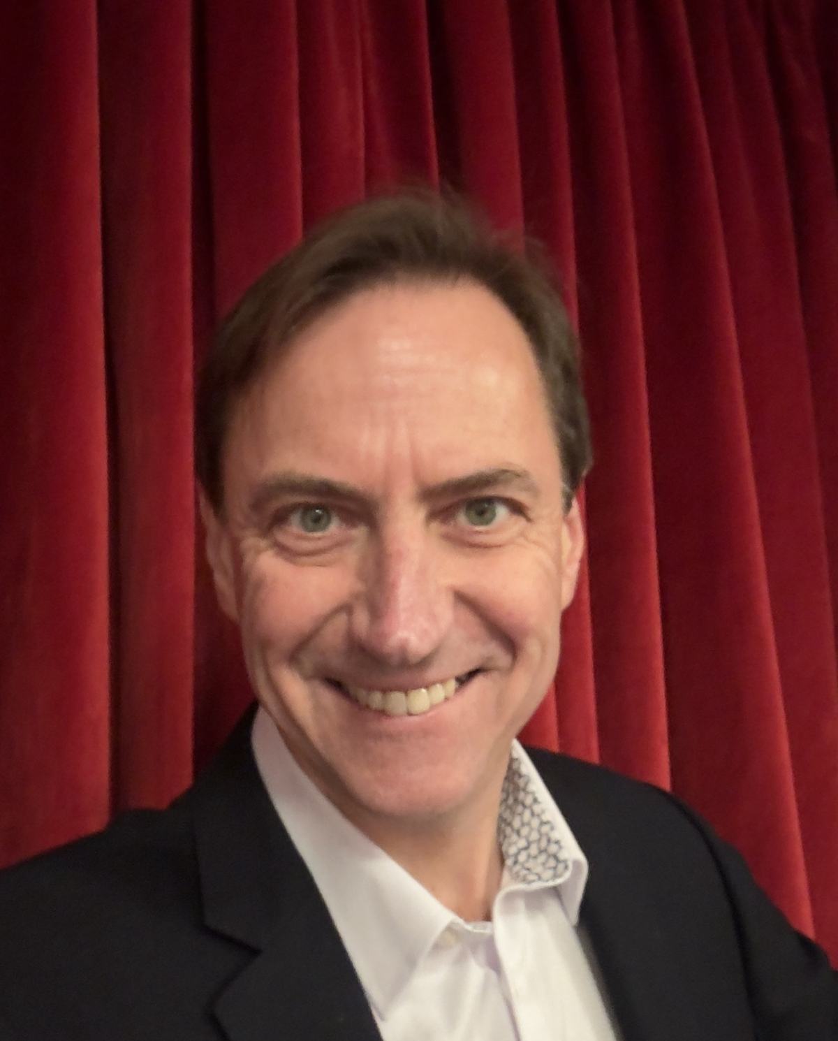 Portrait of Nikolay Klinkov, founder of Fortuna Community, smiling in front of a red curtain